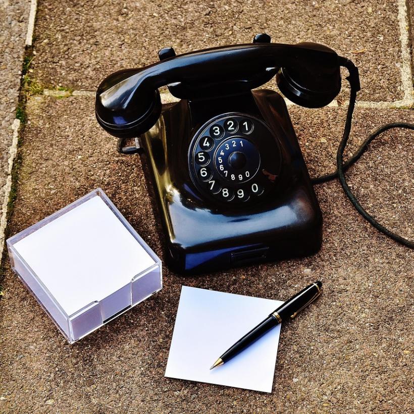 Schwarzes Telefon auf Steinboden, daneben ein Zettelblock und ein Stift